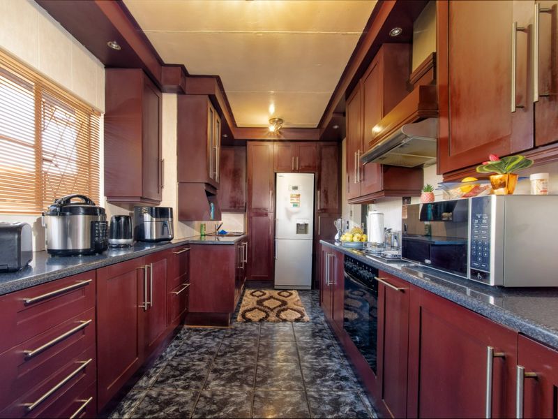 A galley-style kitchen featuring dark wood cabinetry, laminate countertops, built-in oven, extractor fan, and tiled flooring.