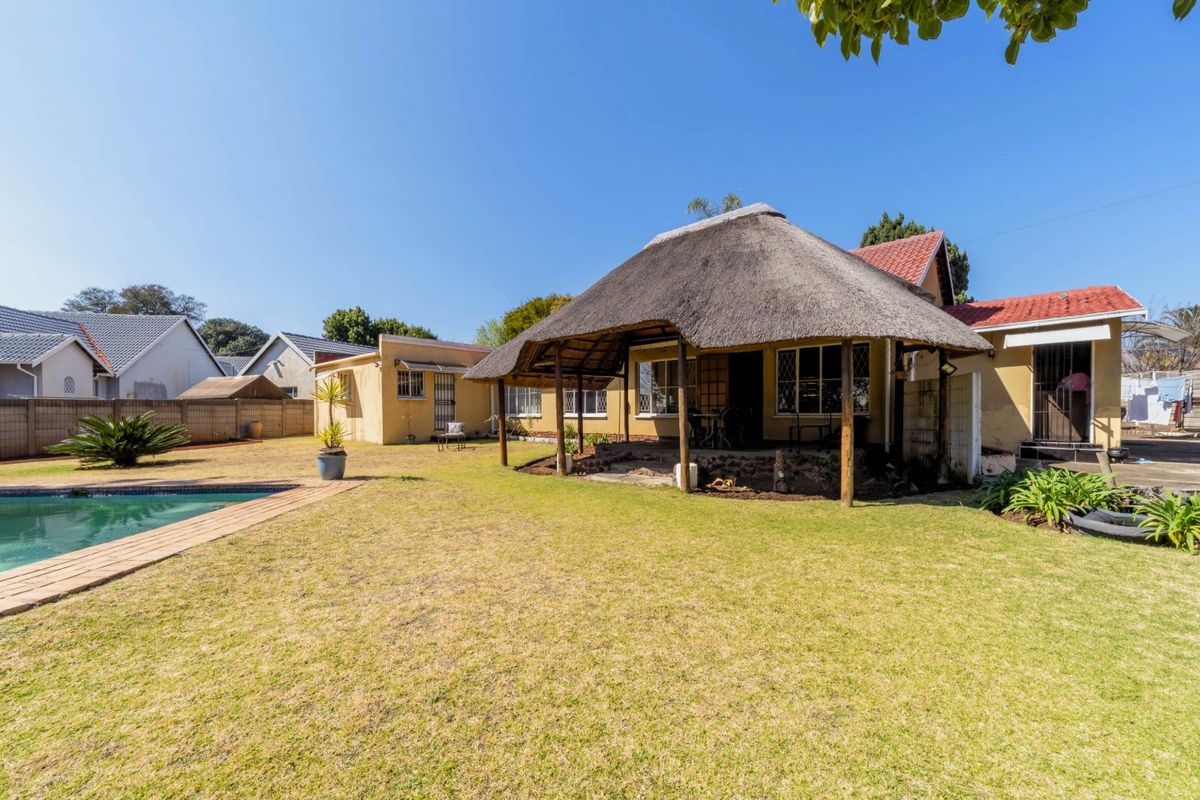 Rear view of the property featuring a thatched roof patio, a swimming pool, and a spacious garden area.