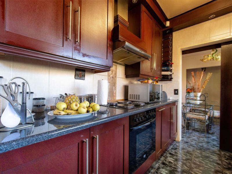 A functional kitchen featuring dark wood cabinetry, granite countertops, a built-in oven, gas hob, and extractor fan with tiled flooring and backsplash.