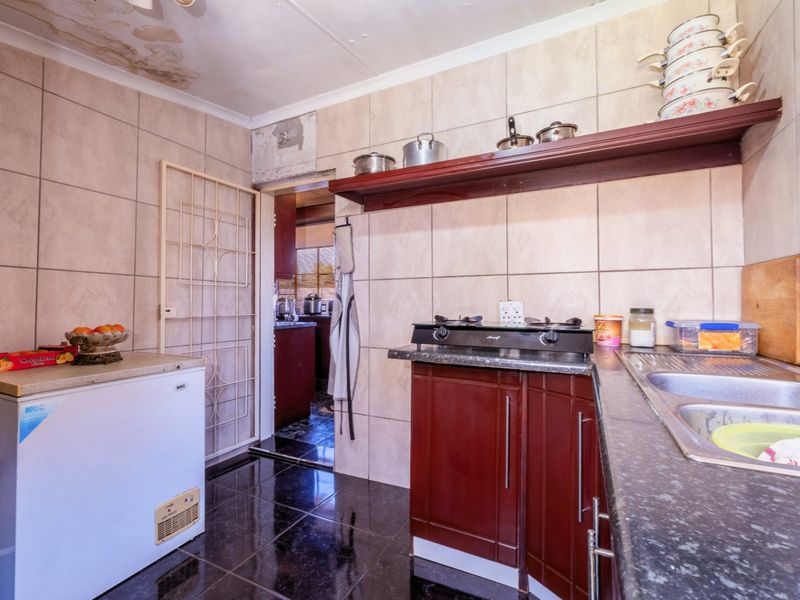 A dated kitchen featuring dark cabinetry, tiled surfaces, and a gas hob, currently showing signs of ceiling water damage and maintenance requirements.