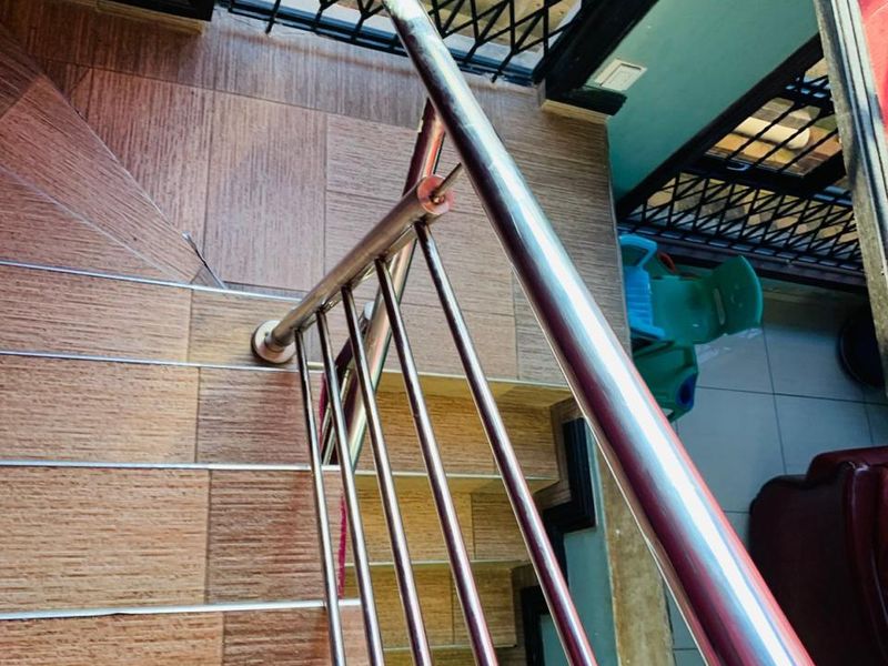 A staircase featuring wood-look tiled steps and a modern stainless steel balustrade, leading to a landing area with a security gate.