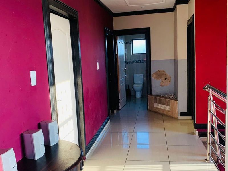 A hallway featuring tiled flooring and a stainless steel balustrade, leading towards a bathroom. The walls show signs of surface damage and peeling paint.