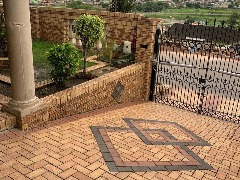 Front entrance area featuring decorative brick paving, a secure wrought iron gate, and a brick boundary wall with a concrete column.