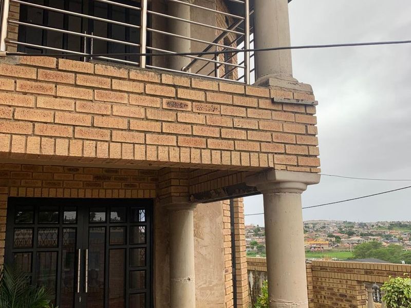 A two-story brick house exterior featuring a balcony with stainless steel railings, concrete columns, and a double glass entrance door.