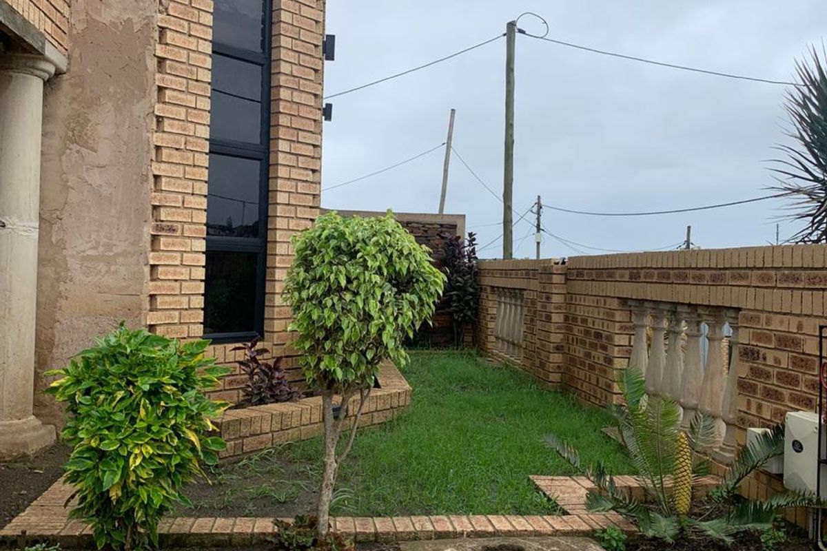 A side garden area featuring face brick retaining walls, a decorative balustrade, and a tall vertical window on the building facade.
