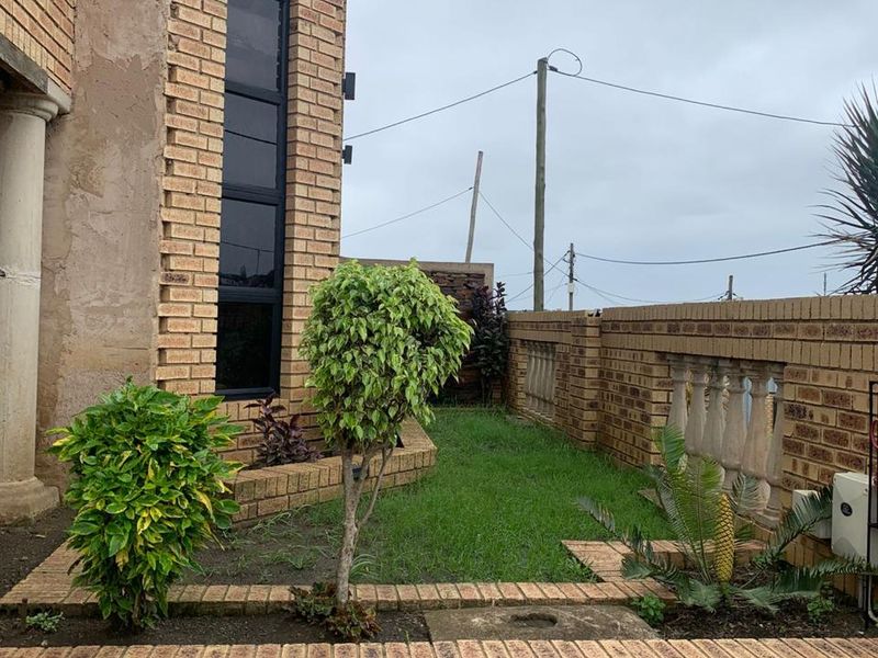 A side garden area featuring face brick retaining walls, a decorative balustrade, and a tall vertical window on the building facade.