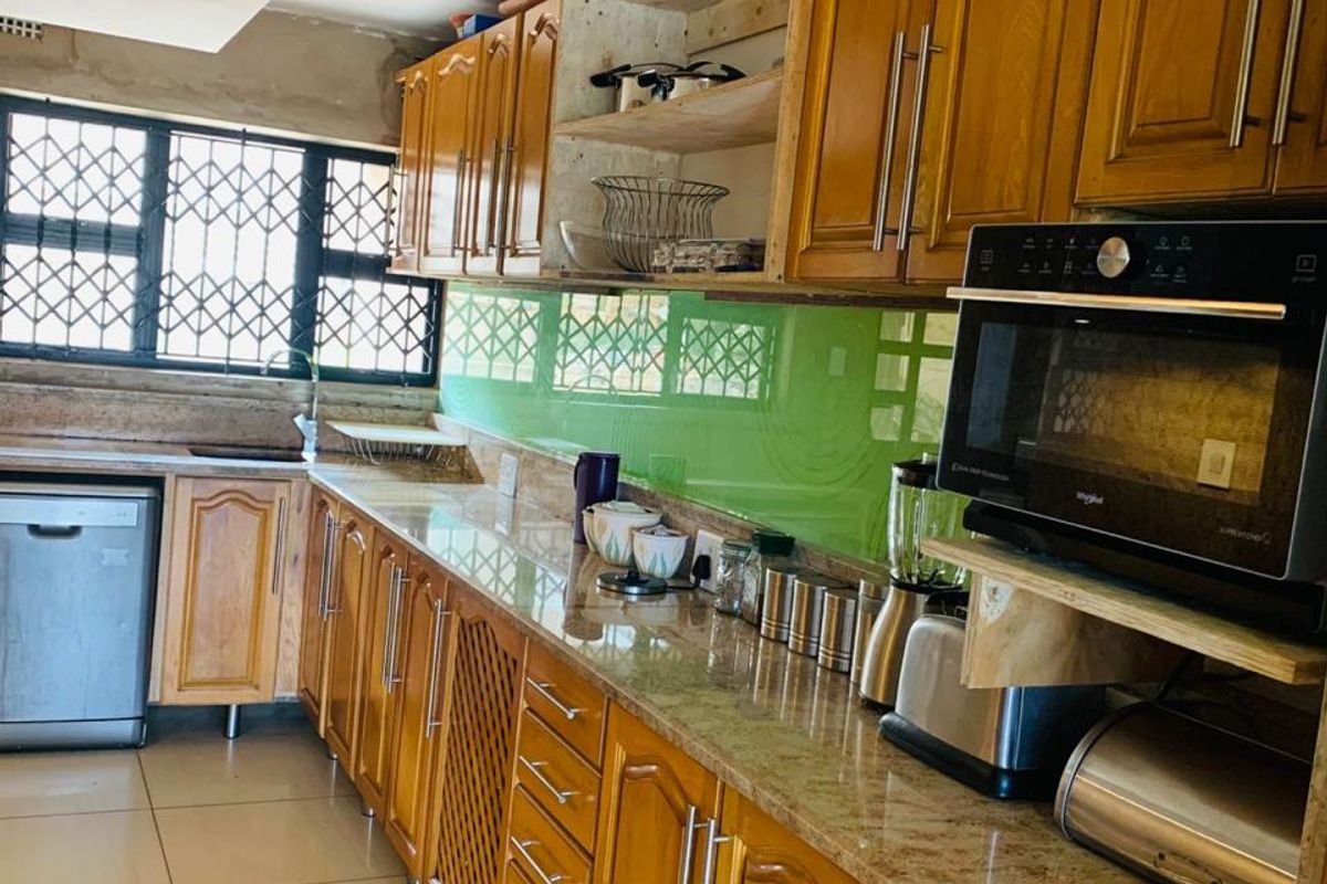 A functional kitchen featuring wooden cabinetry, granite countertops, and a glass splashback, with some areas requiring minor finishing touches.