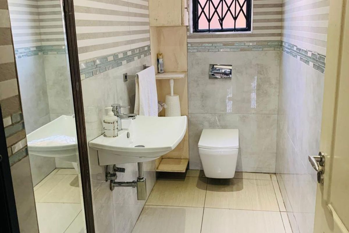 A compact, modern bathroom featuring a wall-mounted basin, wall-hung toilet, and neutral tiled finishes with a secure window.