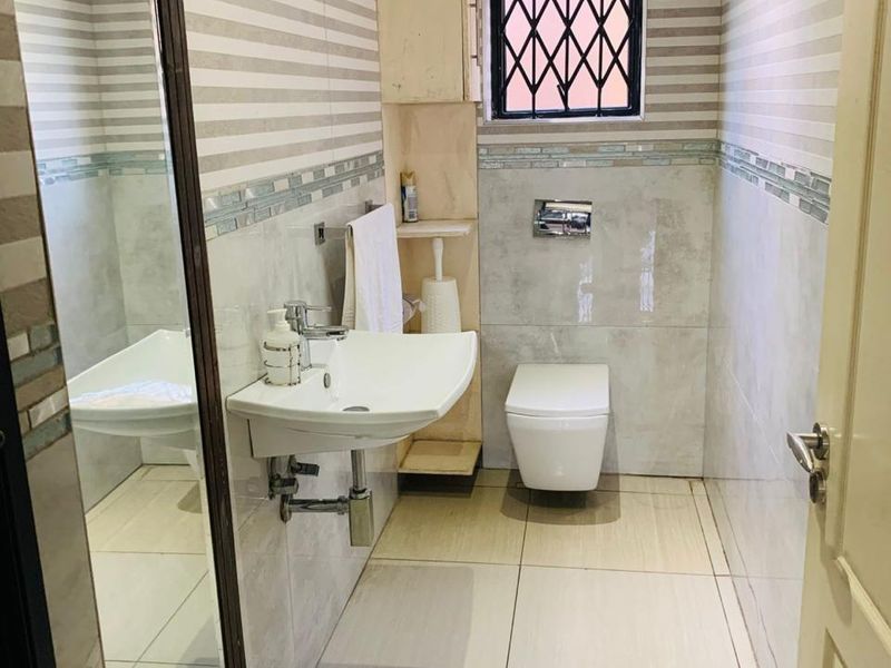 A compact, modern bathroom featuring a wall-mounted basin, wall-hung toilet, and neutral tiled finishes with a secure window.