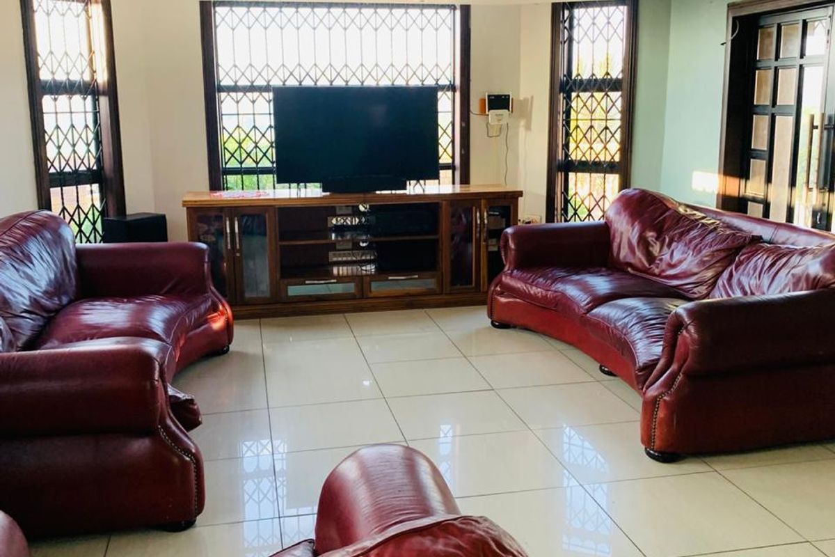 Spacious living room featuring tiled flooring, a coffered ceiling with recessed lighting, and large windows fitted with security bars.