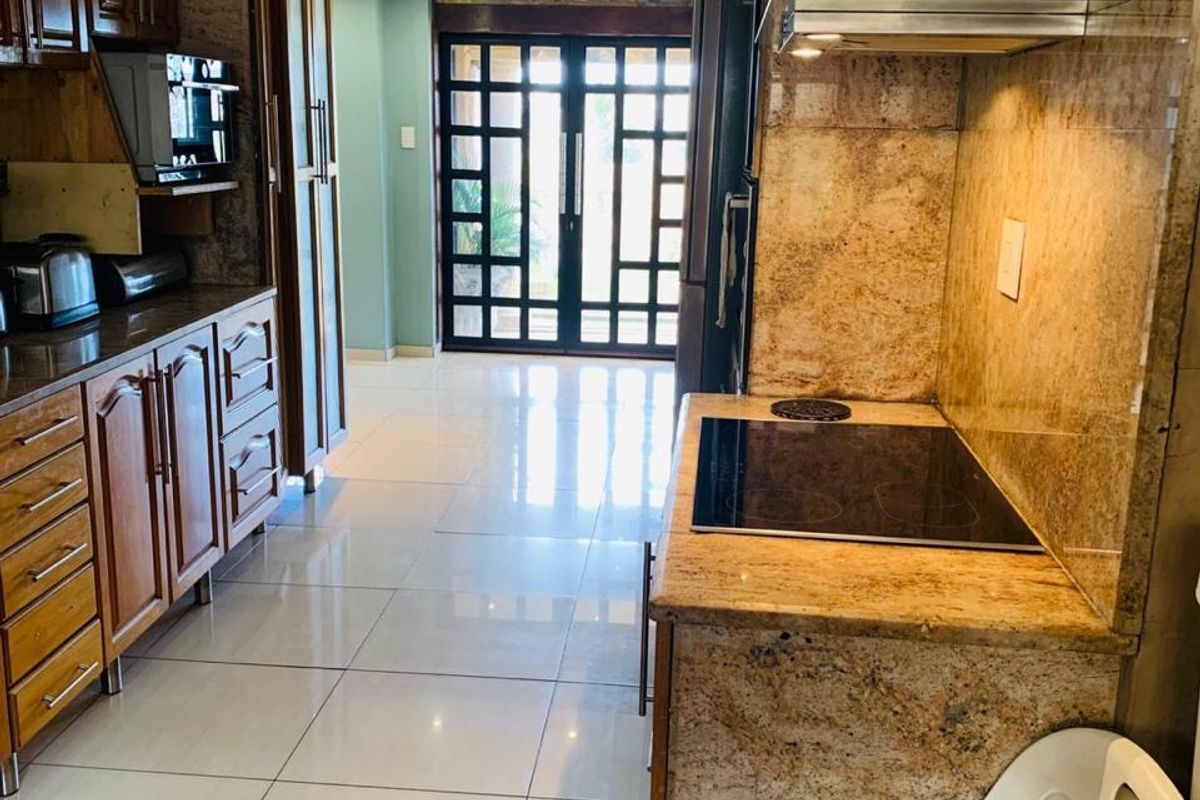 A functional kitchen featuring granite countertops, wooden cabinetry, and integrated appliances, leading through to a bright living area with glass panel doors.