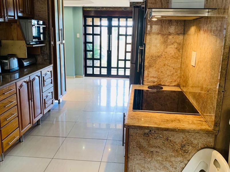 A functional kitchen featuring granite countertops, wooden cabinetry, and integrated appliances, leading through to a bright living area with glass panel doors.