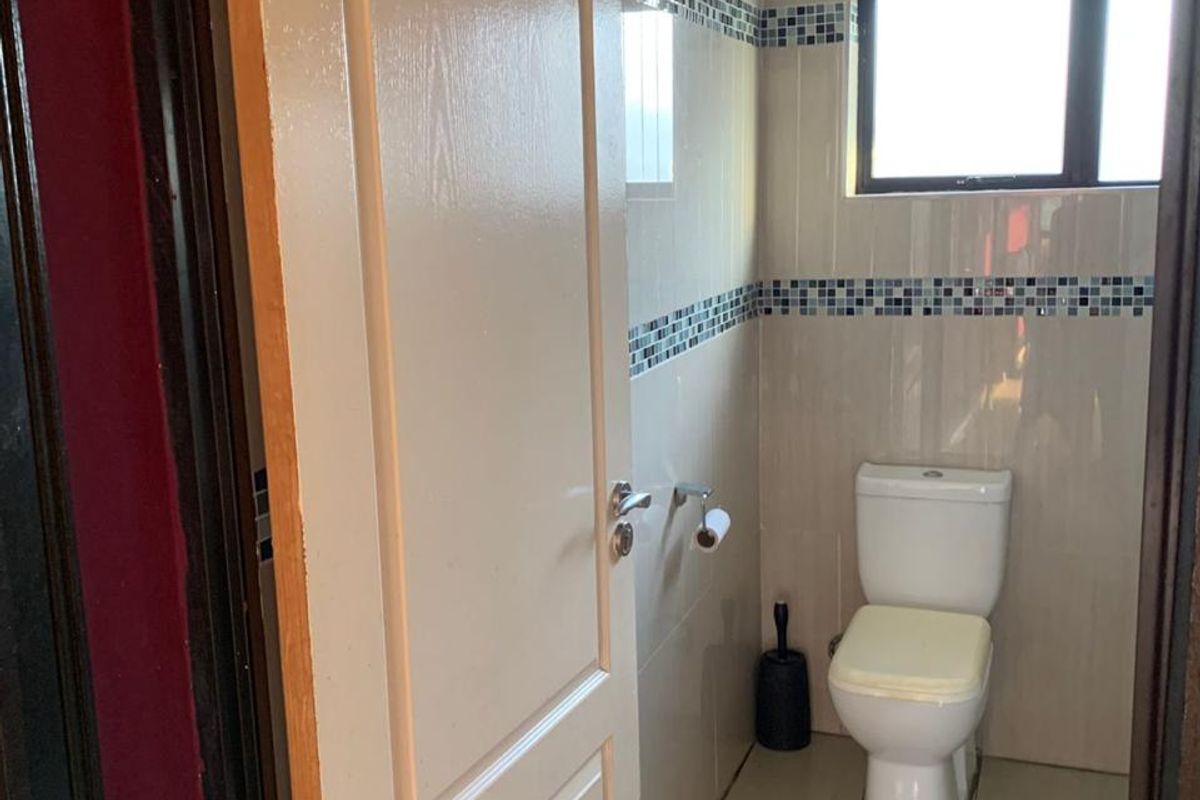 A compact bathroom featuring tiled walls with decorative mosaic accents, tiled flooring, and a standard toilet.