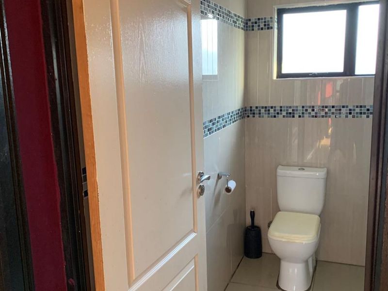 A compact bathroom featuring tiled walls with decorative mosaic accents, tiled flooring, and a standard toilet.