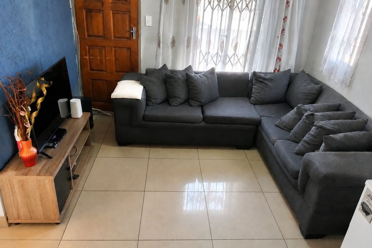 A living room featuring large format floor tiles, a wooden entrance door, and a security gate over the window.