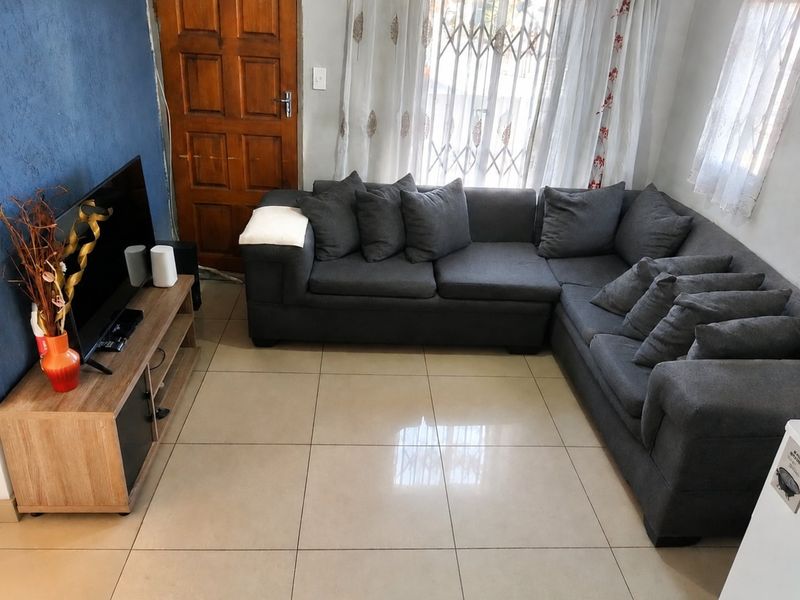 A living room featuring large format floor tiles, a wooden entrance door, and a security gate over the window.