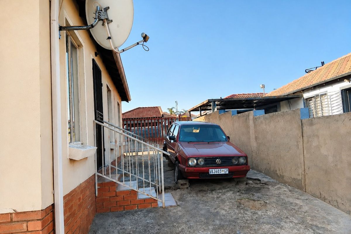 Rear exterior view of the property featuring a concrete driveway, boundary wall, and metal security access gate.