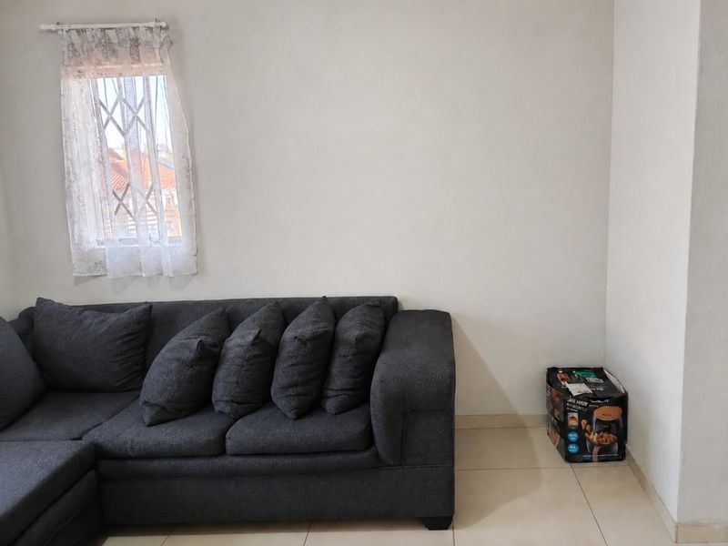 A living room area featuring neutral tiled flooring and a window fitted with a security gate.