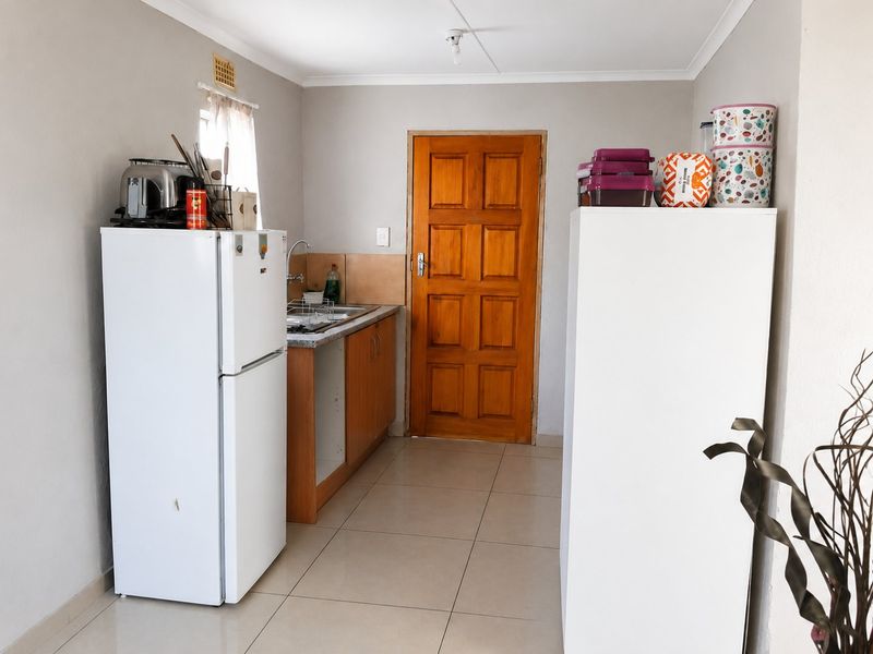 A functional kitchen area featuring tiled flooring, wooden cabinetry, and a solid timber door, providing a practical space for food preparation.