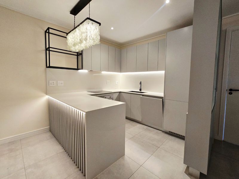 Modern, minimalist kitchen featuring sleek handleless cabinetry, stone countertops, integrated appliances, and a stylish slatted breakfast bar with ambient under-counter lighting.