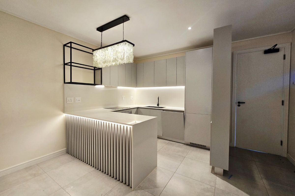 Modern, minimalist kitchen featuring sleek handleless cabinetry, stone countertops, integrated appliances, and a stylish breakfast bar with under-counter lighting.
