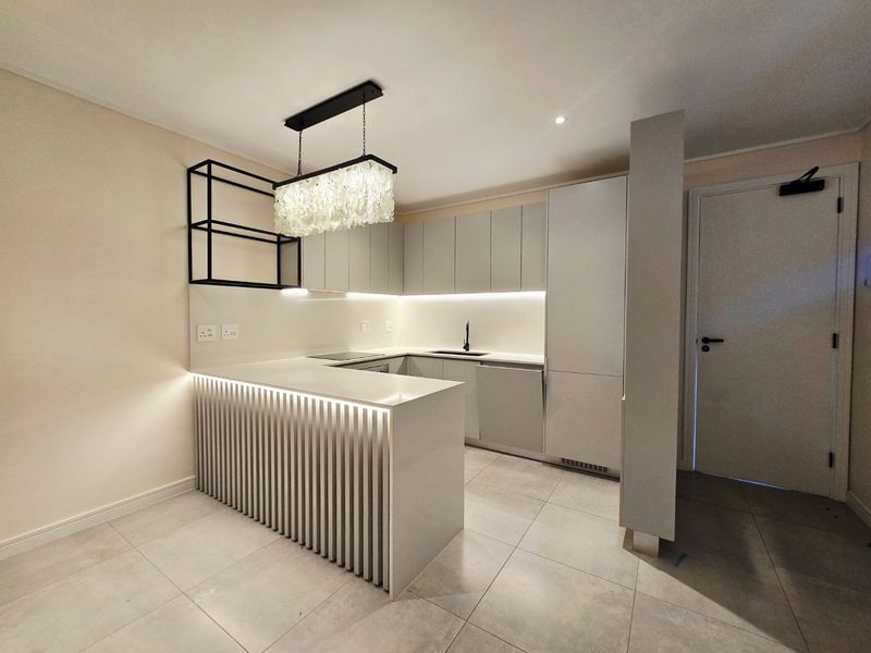 Modern, minimalist kitchen featuring sleek handleless cabinetry, stone countertops, integrated appliances, and a stylish breakfast bar with under-counter lighting.