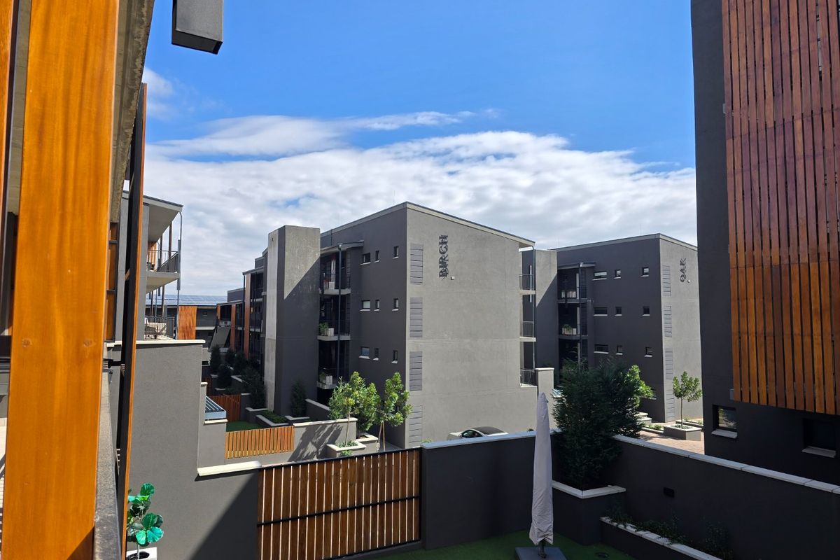 View of the apartment complex exterior, featuring modern grey facades, timber accents, and a private balcony area with artificial turf.
