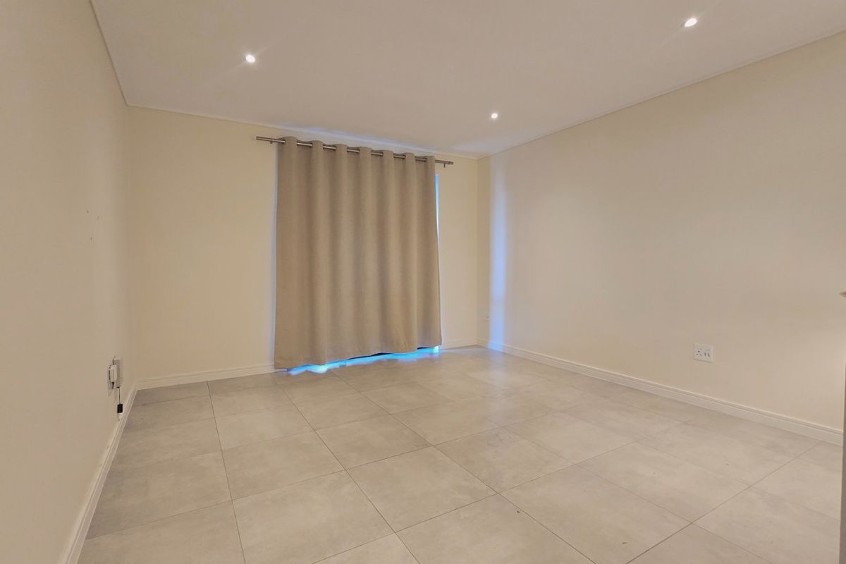 A bright, empty living room featuring neutral tiled flooring, recessed downlighting, and clean wall finishes, ready for personalization.