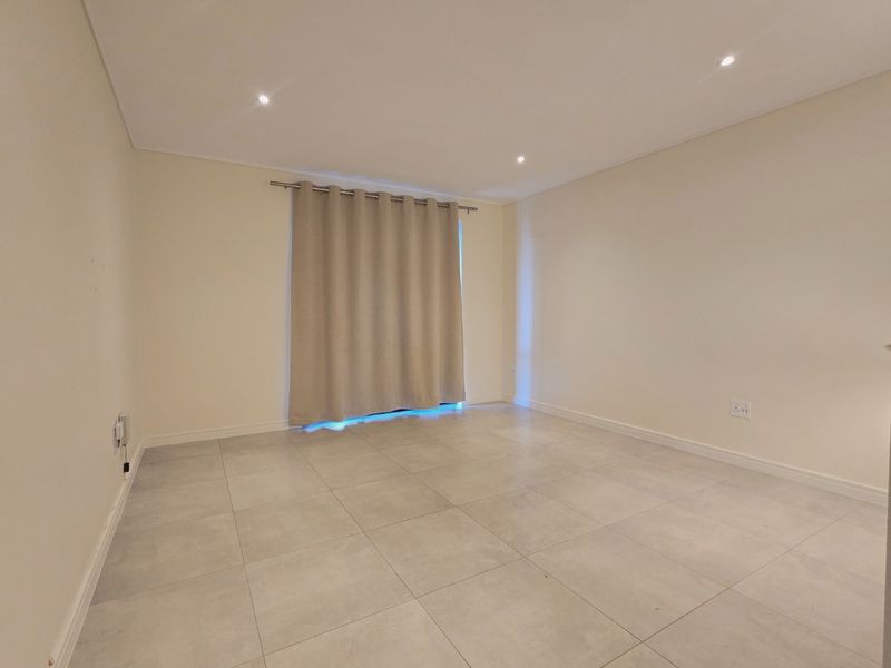 A bright, empty living room featuring neutral tiled flooring, recessed downlighting, and clean wall finishes, ready for personalization.