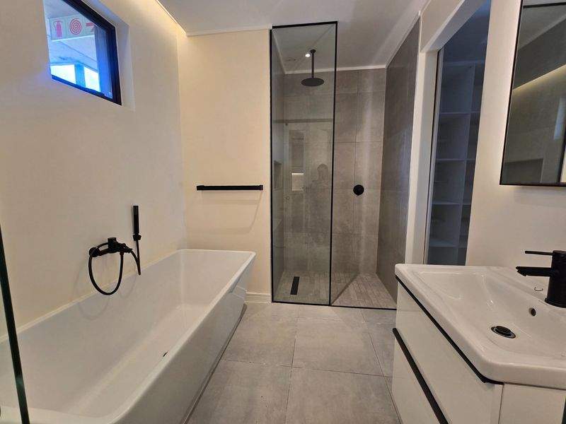 Modern bathroom featuring a sleek freestanding bathtub, a spacious walk-in shower with black matte fixtures, and a contemporary vanity unit.