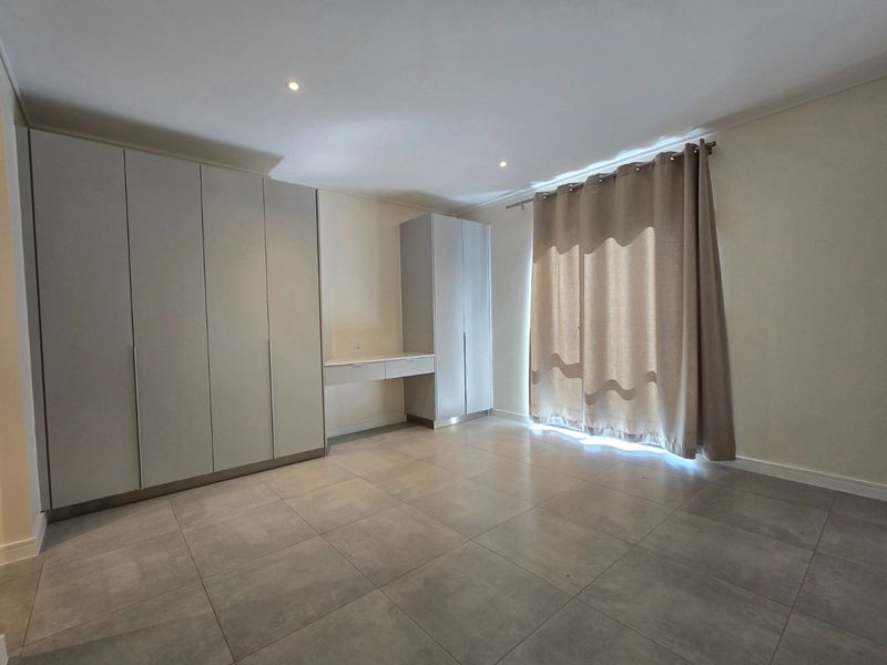 A spacious bedroom featuring neutral tiled flooring, extensive built-in cabinetry with an integrated desk, and recessed lighting.