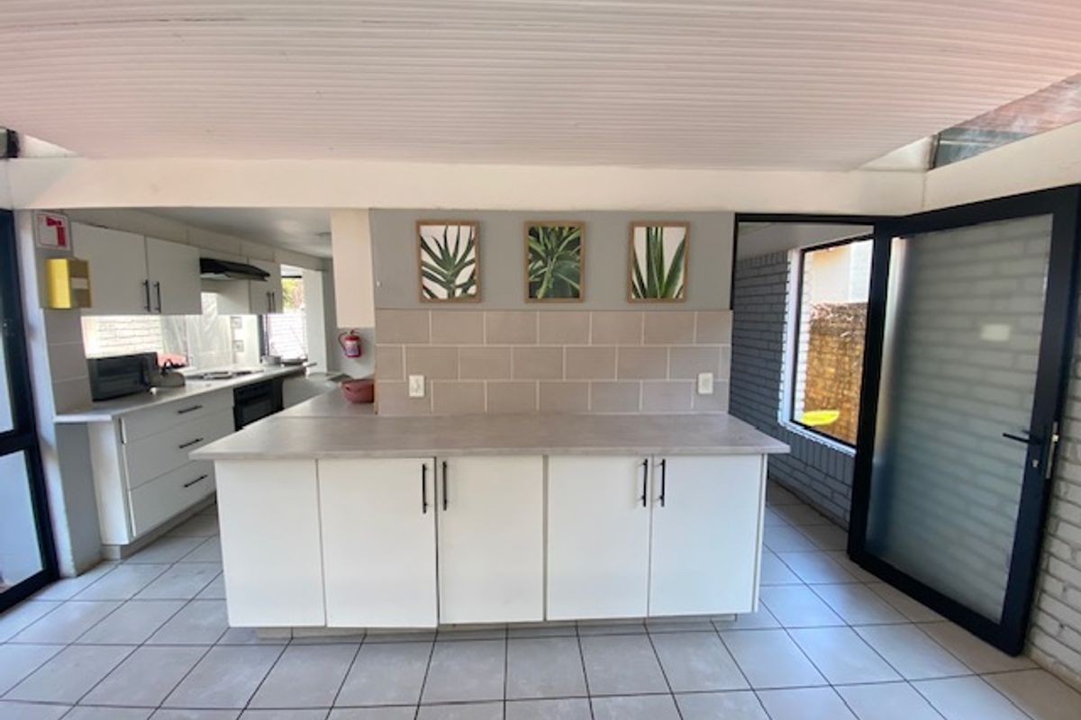 Modernized kitchen featuring white cabinetry, neutral tiled backsplash, and a central island, with direct access to an outdoor area through a glass door.