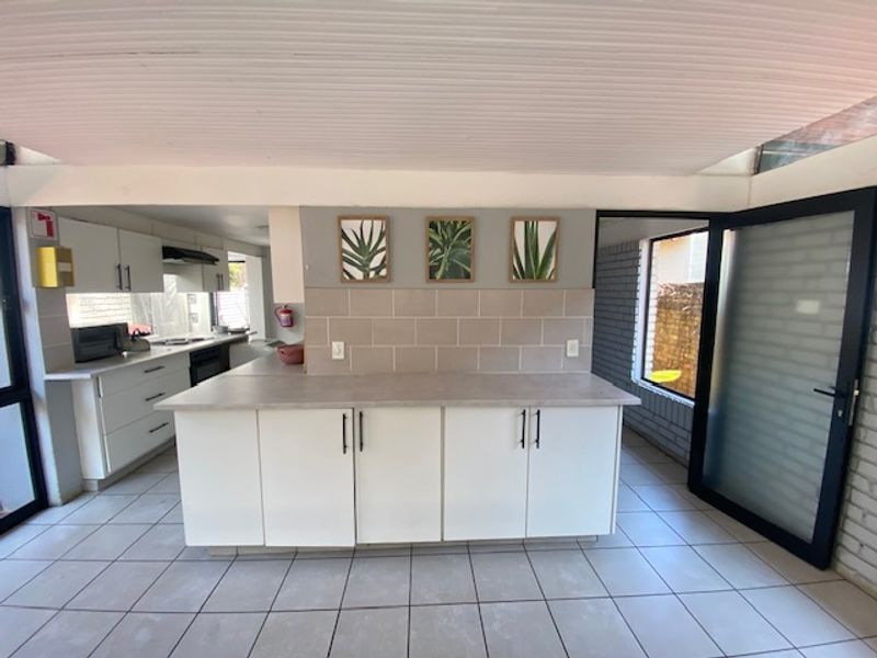 Modernized kitchen featuring white cabinetry, neutral tiled backsplash, and a central island, with direct access to an outdoor area through a glass door.