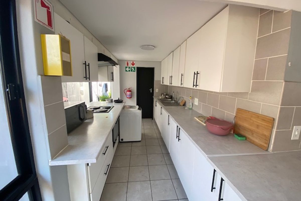 A functional galley-style kitchen featuring white cabinetry, tiled backsplash, laminate countertops, and integrated appliances with tiled flooring throughout.