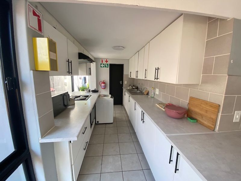 A functional galley-style kitchen featuring white cabinetry, tiled backsplash, laminate countertops, and integrated appliances with tiled flooring throughout.