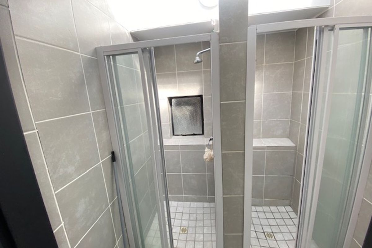 A functional bathroom featuring dual shower stalls with modern grey tiling, glass enclosures, and built-in shower niches for storage.