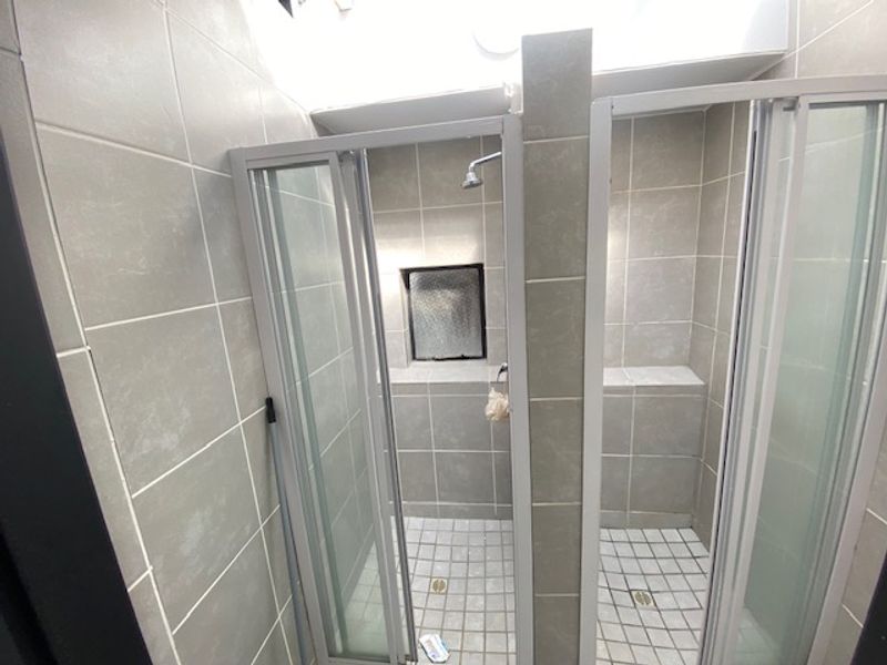 A functional bathroom featuring dual shower stalls with modern grey tiling, glass enclosures, and built-in shower niches for storage.
