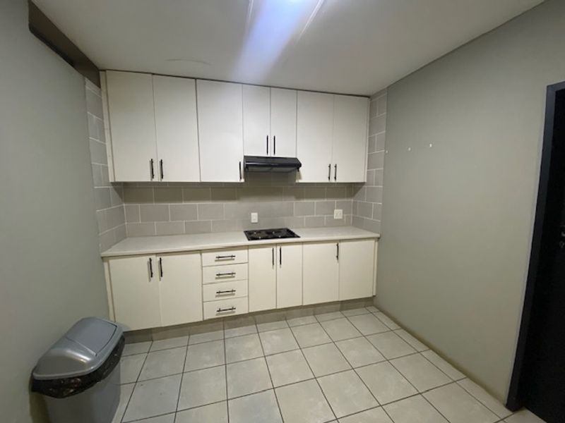A clean, functional kitchen featuring white built-in cabinetry, a hob with extractor fan, tiled splashback, and neutral tiled flooring.