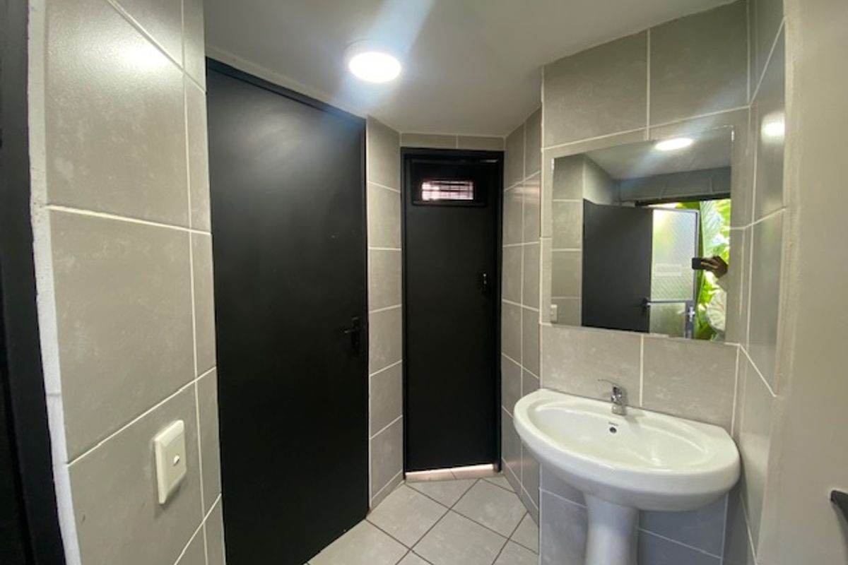 A compact bathroom featuring neutral wall tiles, a pedestal basin, and a wall-mounted mirror with contrasting dark doors.