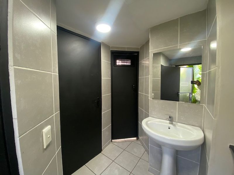 A compact bathroom featuring neutral wall tiles, a pedestal basin, and a wall-mounted mirror with contrasting dark doors.