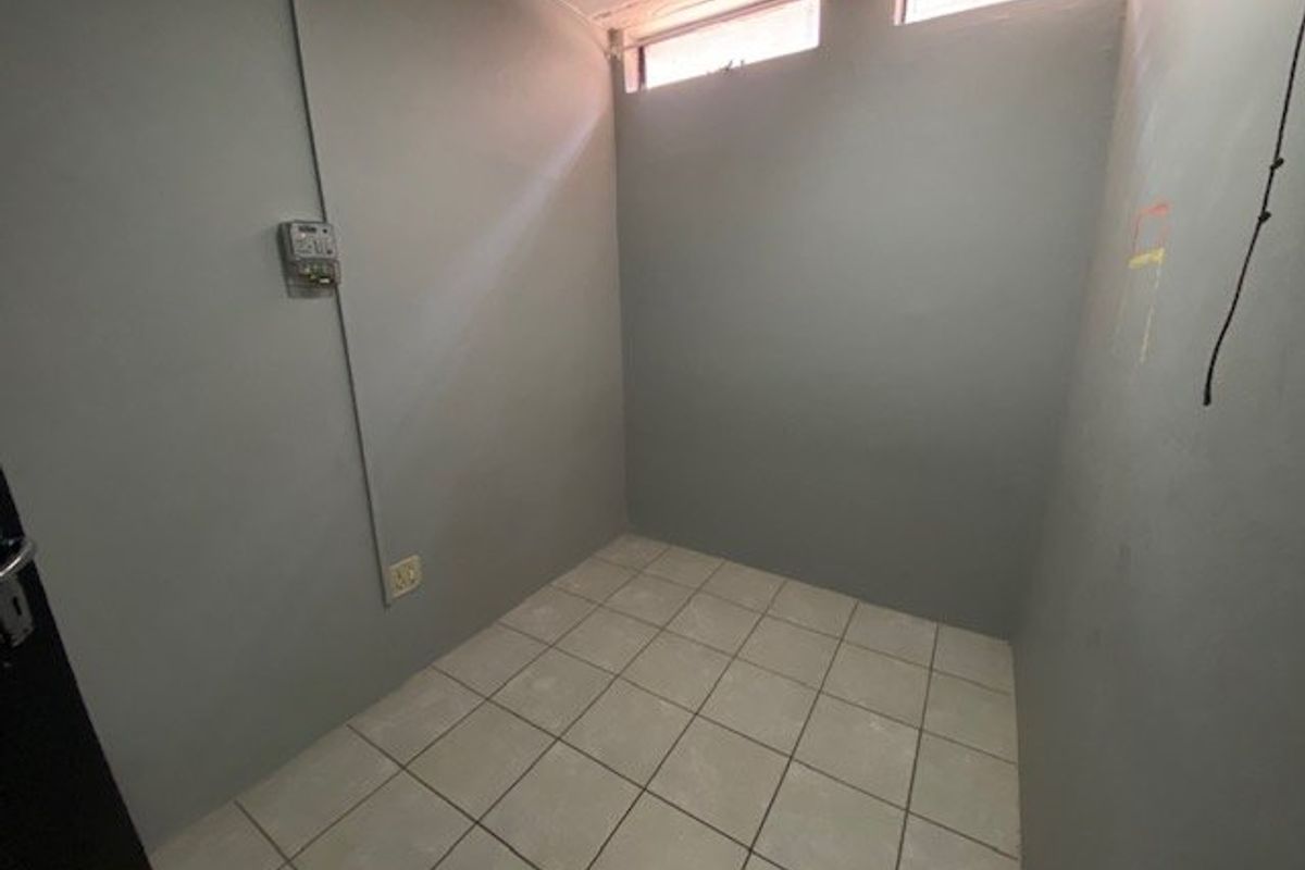 A small, empty utility space featuring tiled flooring, high-level clerestory windows, and an exposed electrical distribution board.