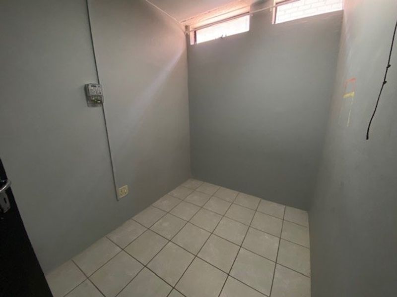 A small, empty utility space featuring tiled flooring, high-level clerestory windows, and an exposed electrical distribution board.