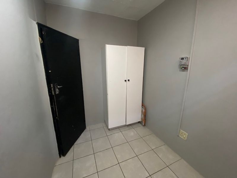 A functional utility space featuring tiled flooring, a security alarm keypad, and neutral wall finishes, suitable for storage or a home office setup.