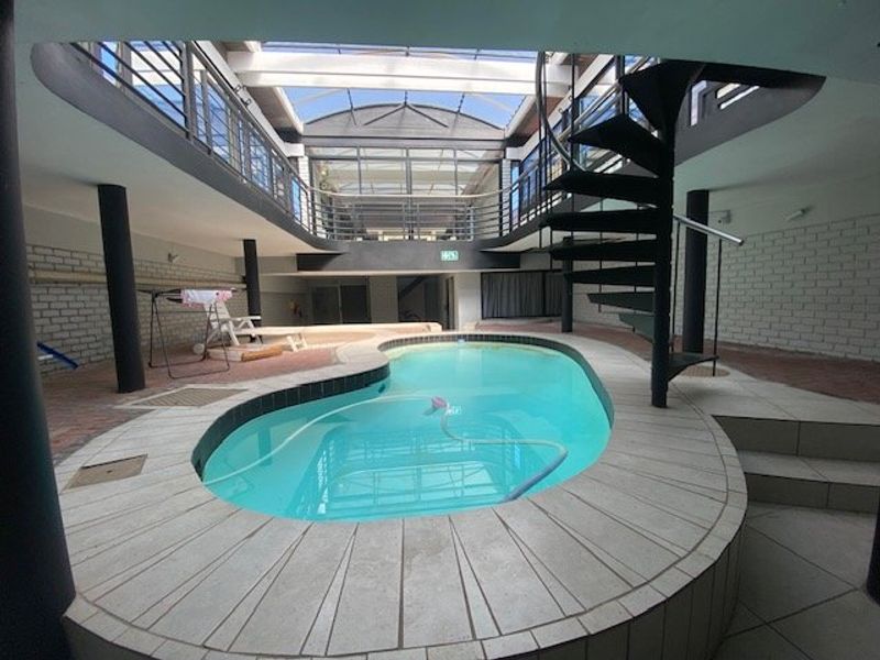 Unique indoor swimming pool area featuring a central pool, spiral staircase, and a large skylight providing natural light to the surrounding mezzanine level.
