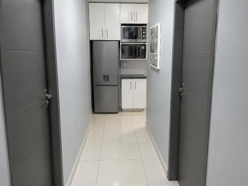 A clean, modern scullery or utility area featuring white built-in cabinetry, tiled flooring, and grey internal doors.