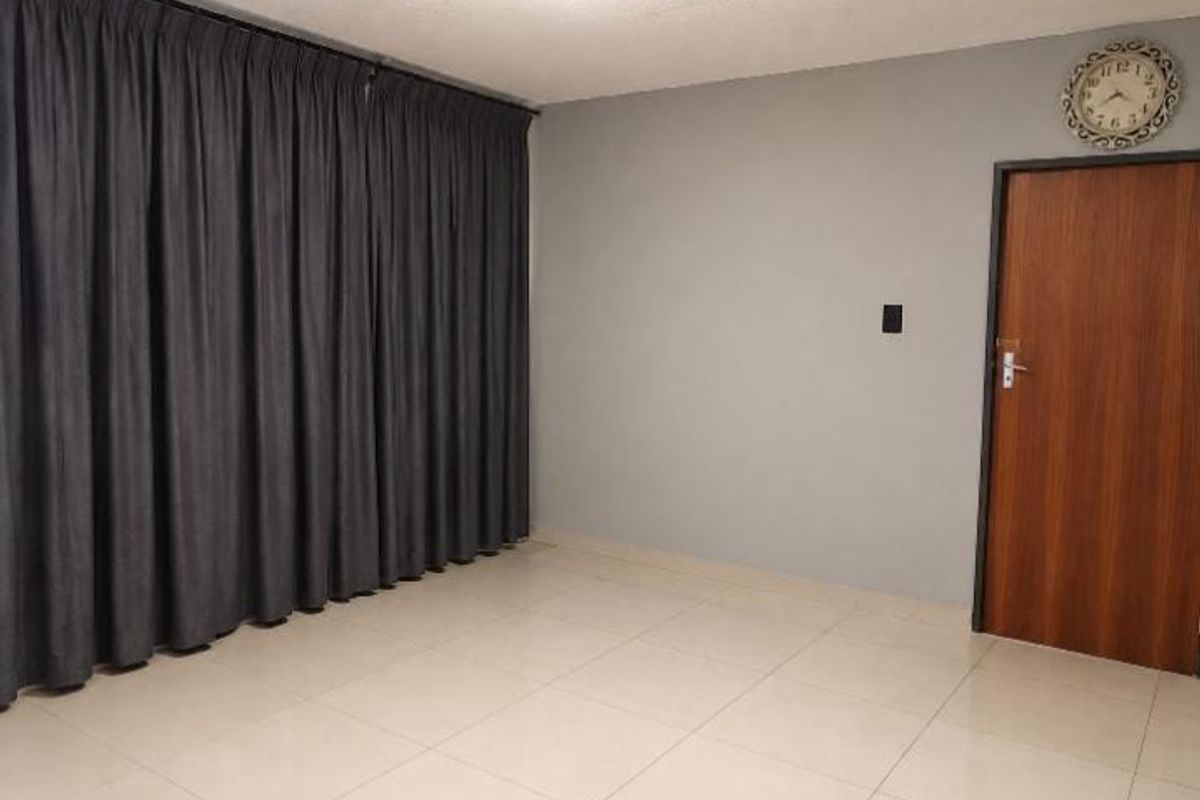 An empty living room featuring neutral tiled flooring, grey painted walls, and a wooden door.