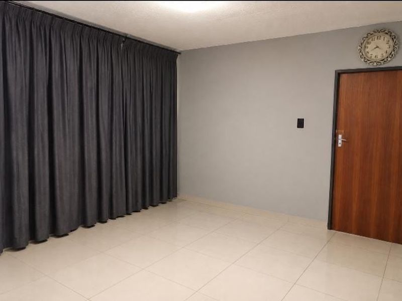 An empty living room featuring neutral tiled flooring, grey painted walls, and a wooden door.