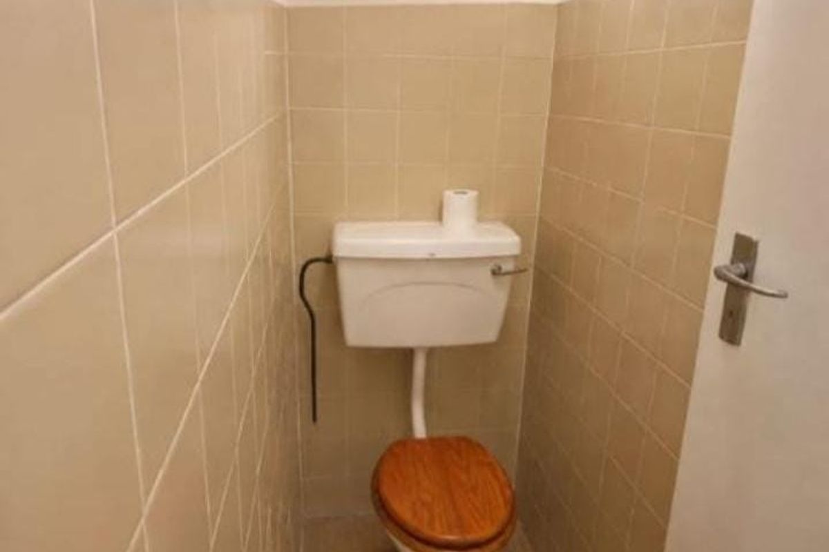 A small, dated bathroom featuring beige wall tiles and a standard toilet with exposed plumbing.