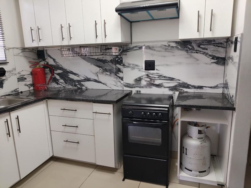 A functional kitchen featuring white cabinetry, granite countertops, a marble-look splashback, and a freestanding oven with an extractor fan.