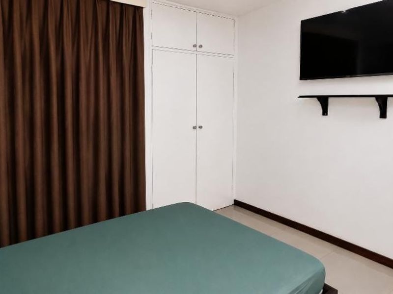 A functional bedroom featuring built-in wardrobe storage, tiled flooring, and a wall-mounted shelf for media equipment.